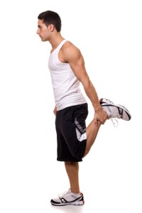 Man standing upright in sports wear holding ankle of raised leg